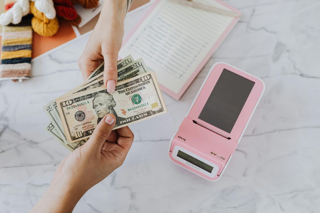 Close-up of hands exchanging US dollars with a pink calculator on a marble surface.