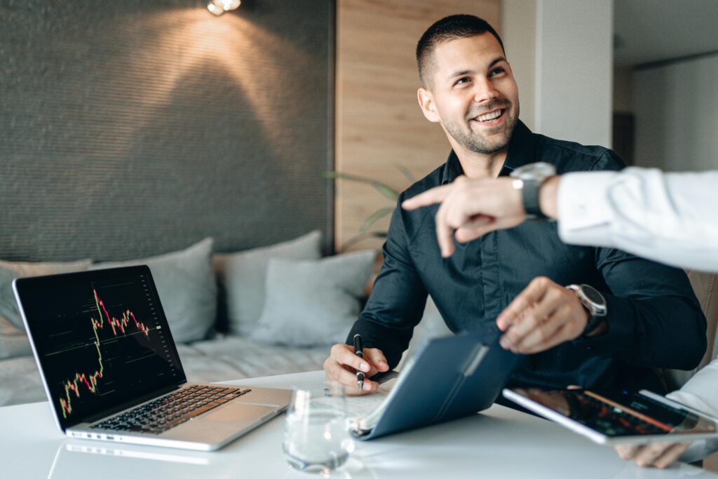 Smiling businessmen discussing data on laptops during a meeting at a stylish office.