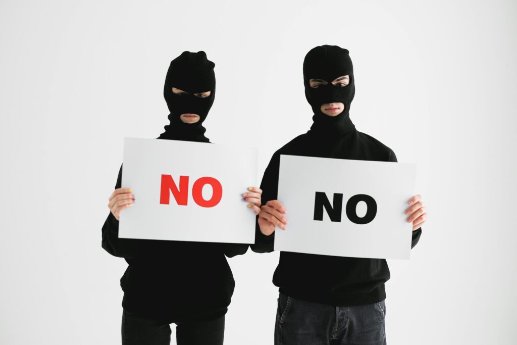 Two masked individuals holding "No" signs against a white background, concept of refusal or anonymity.